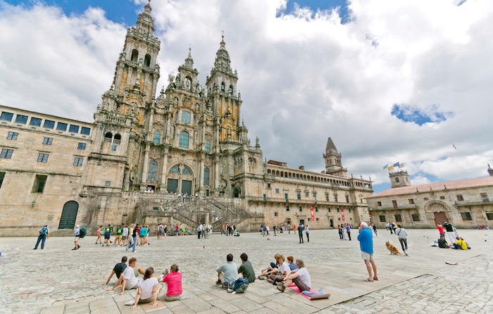 Pellegrini seduti a gruppi o in piedi contemplano la facciata della cattedrale di Santiago de Compostela dalla piazza dell'Obradoiro.